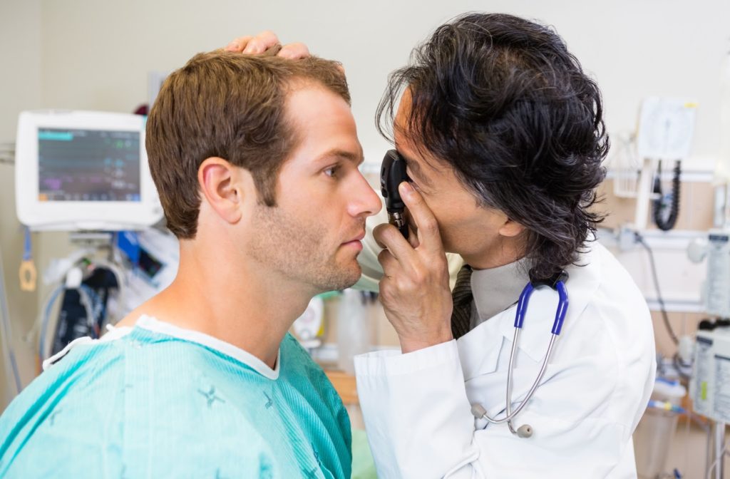 Optometrist with ophthalmoscope examining patient's eye
