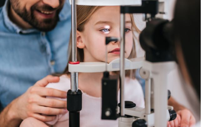 Young girl with father at eye doctors office undergoing eye exam to look for myopia