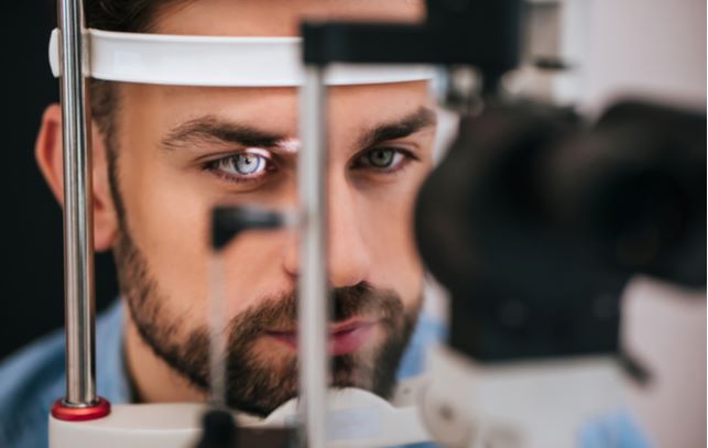 man at optometrist office having eyes checked out with flashed light into eye