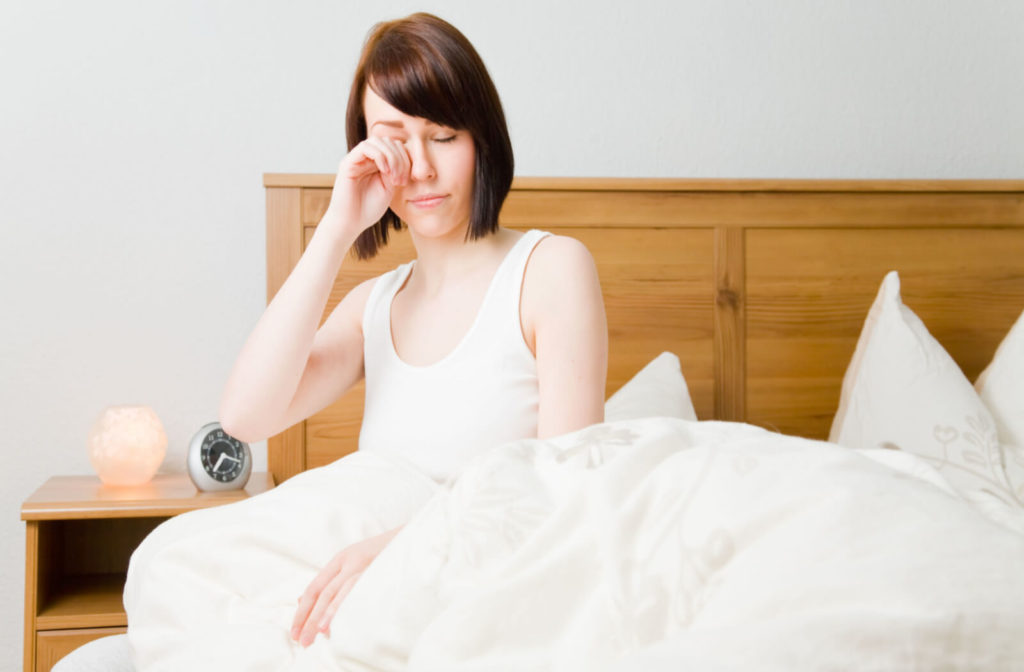 a woman in bed rubs her eyes because she woke up with dry eyes