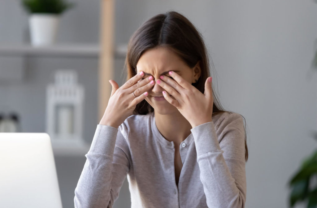 a teen girl is rubbing her dry and irritable eyes and feels eye strain and tension migraines after computer work