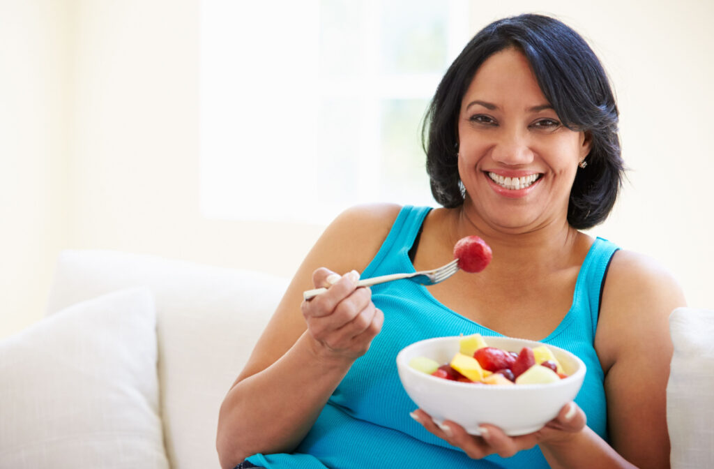 A woman sitting on a couch eating a bowl of fruits.