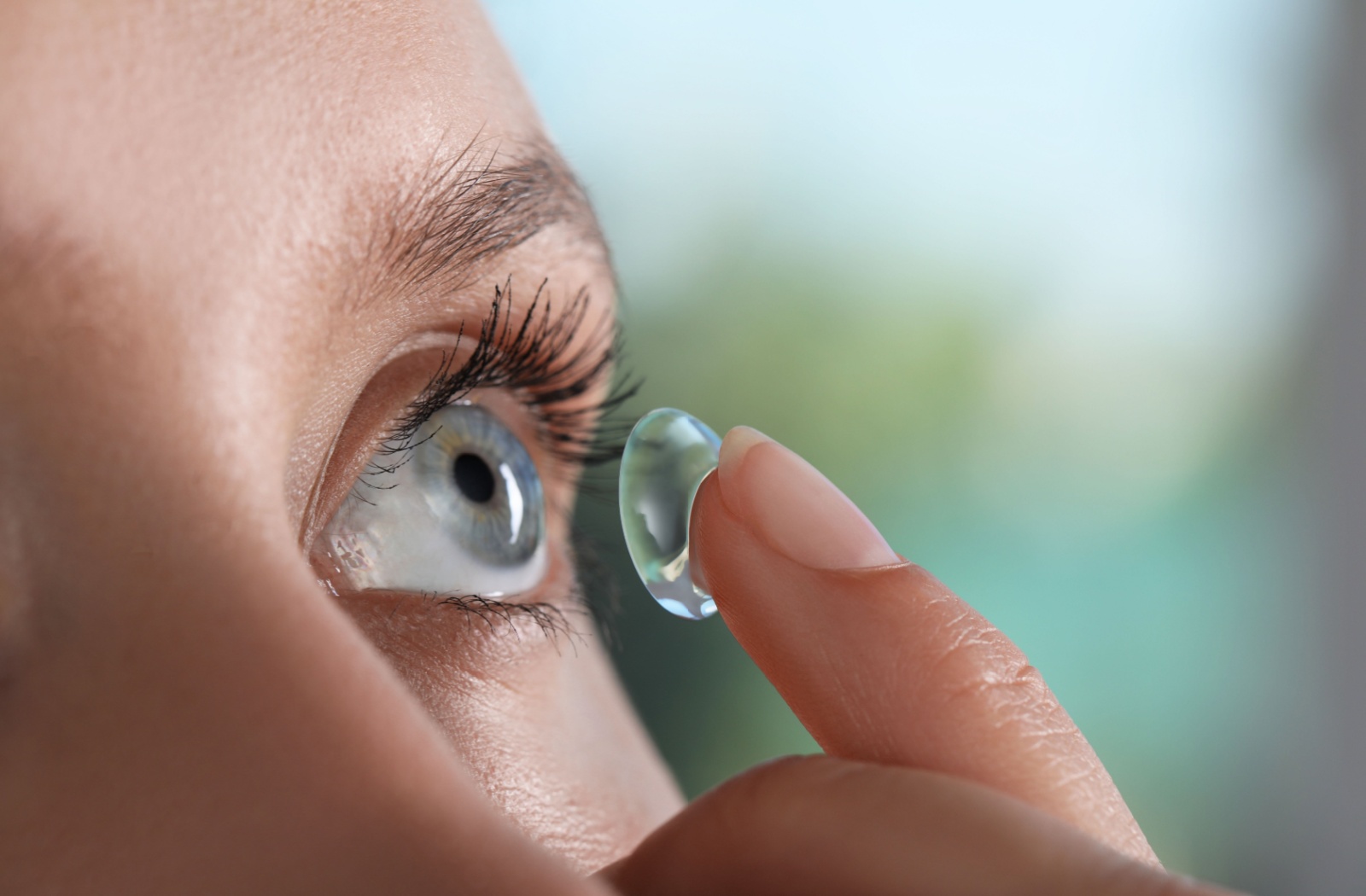 Close-up of a woman placing a contact lens into her left eye with her index finger