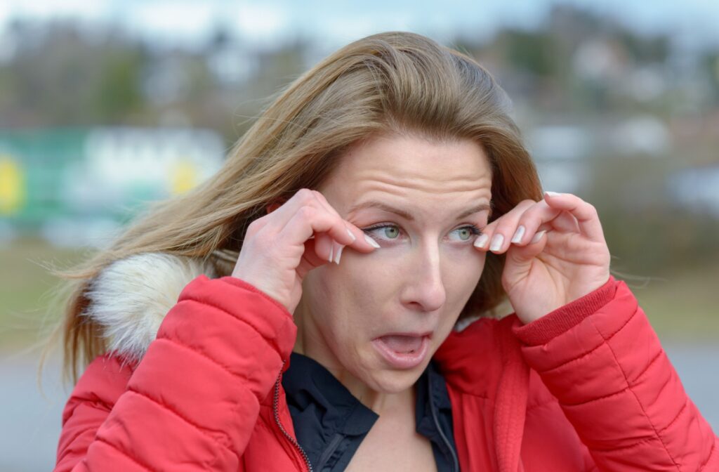 A woman in the cold outdoors dabs at her overly watery eyes.
