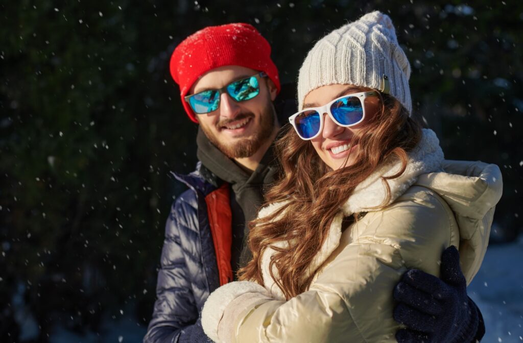 A smiling couple out in the snow, wearing sunglasses to protect their eyes from cold weather.
