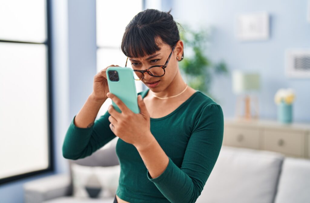 Woman wearing glasses tipped down, squinting while trying to read her phone.