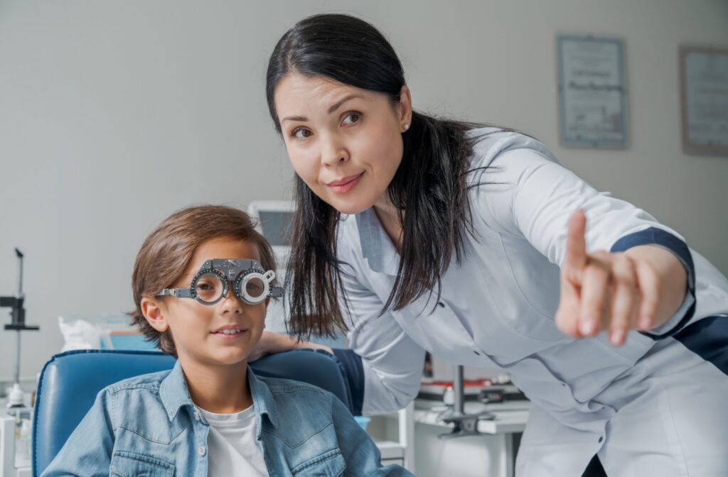 Young patient undergoing an eye exam with a diagnostic tool while optometrist points to a visual aid.