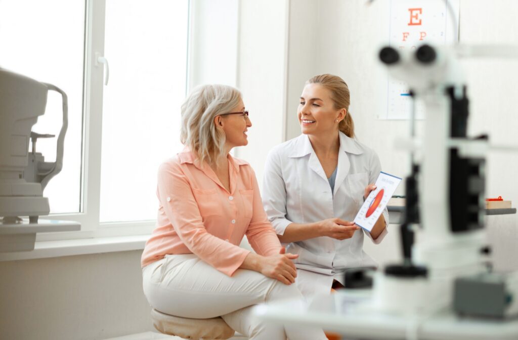 A patient and an eye care professional sit together in an exam room, smiling while reviewing an eye chart diagram.