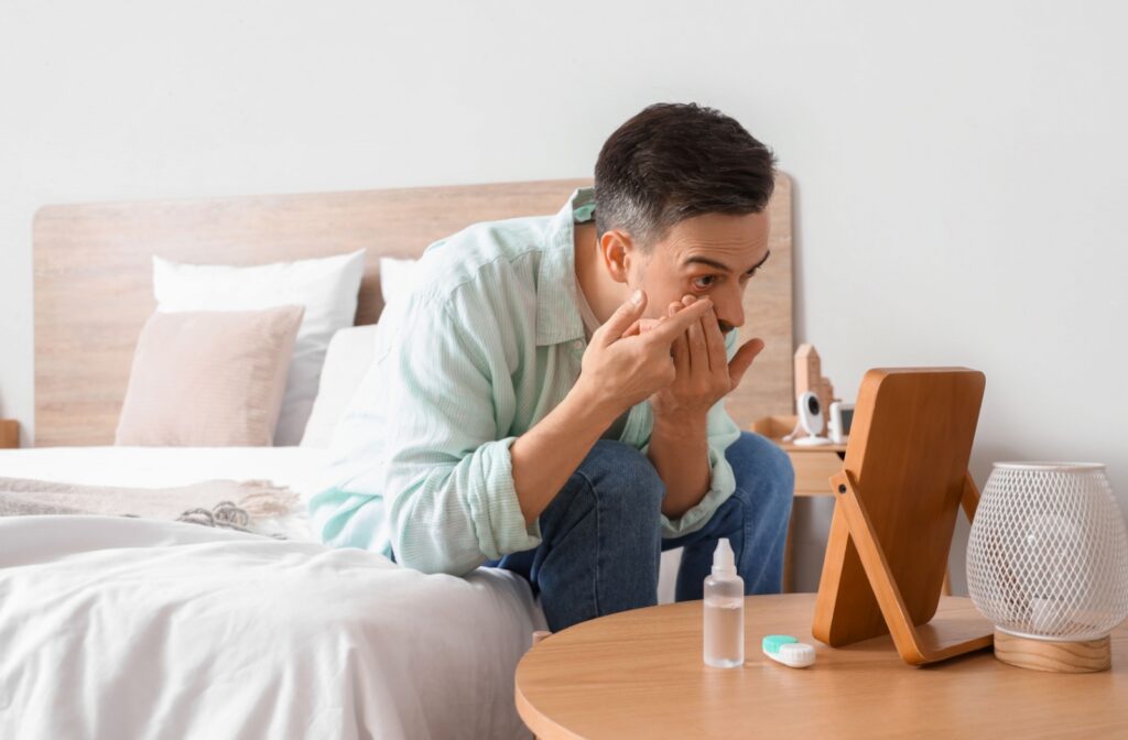 A person leans over to look into a mirror while they put contacts into their eye