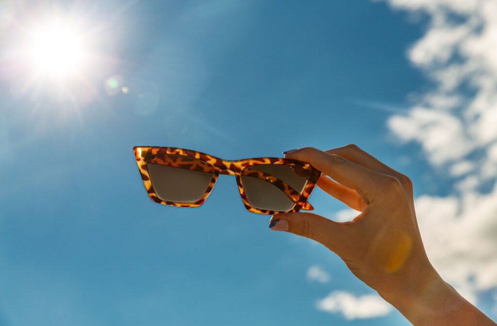 A pair of sunglasses being held up to the sun and blue sky