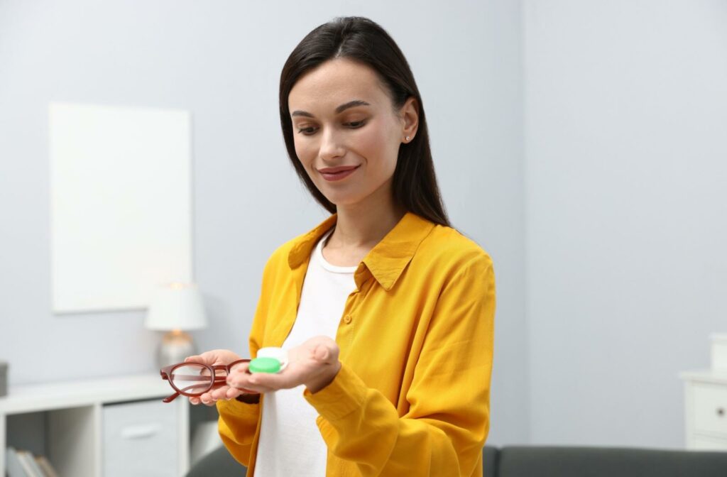 A person holding a contact lens case in one hand and a pair of glasses in the other hand